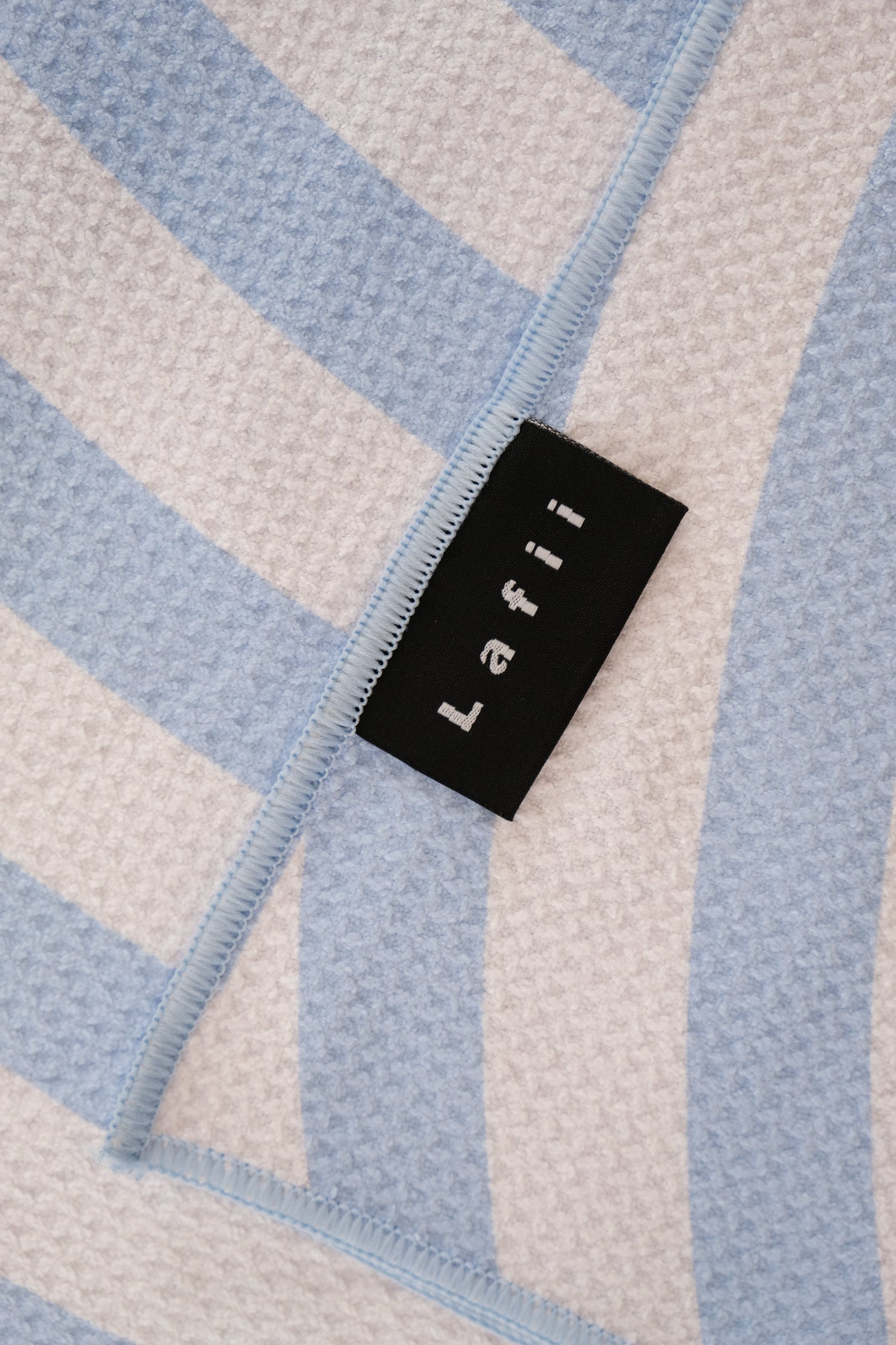 Close-up van het Lafii-label op een blauw-wit microvezel strandlaken – hoogwaardige afwerking met geweven merklabel en zachte wafelstructuur.